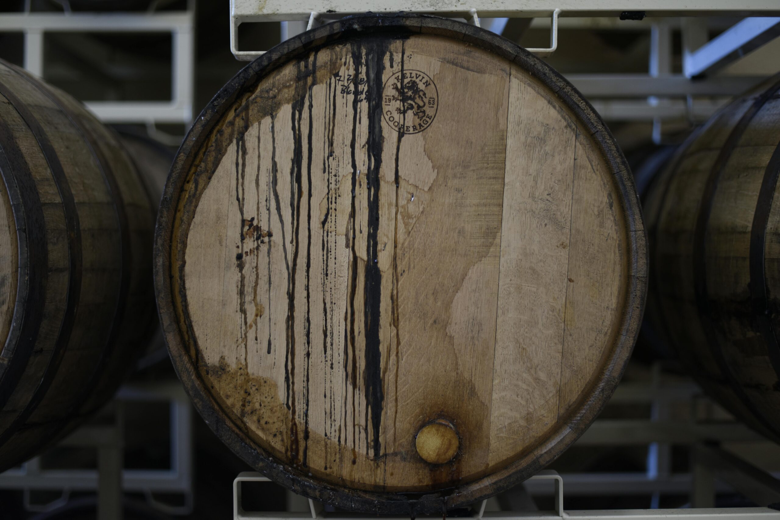 An oak barrel in a brewery cellar with dark liquid stains, ideal for themes of fermentation and distilling.
