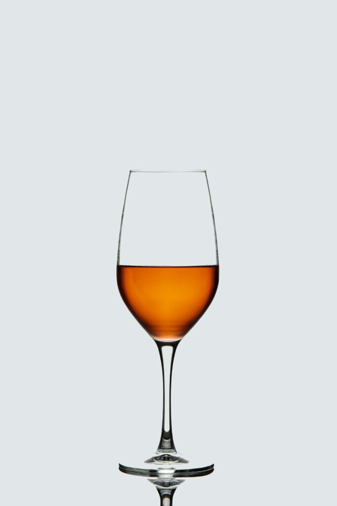 A clear glass filled with orange wine against a minimalist, pale backdrop.