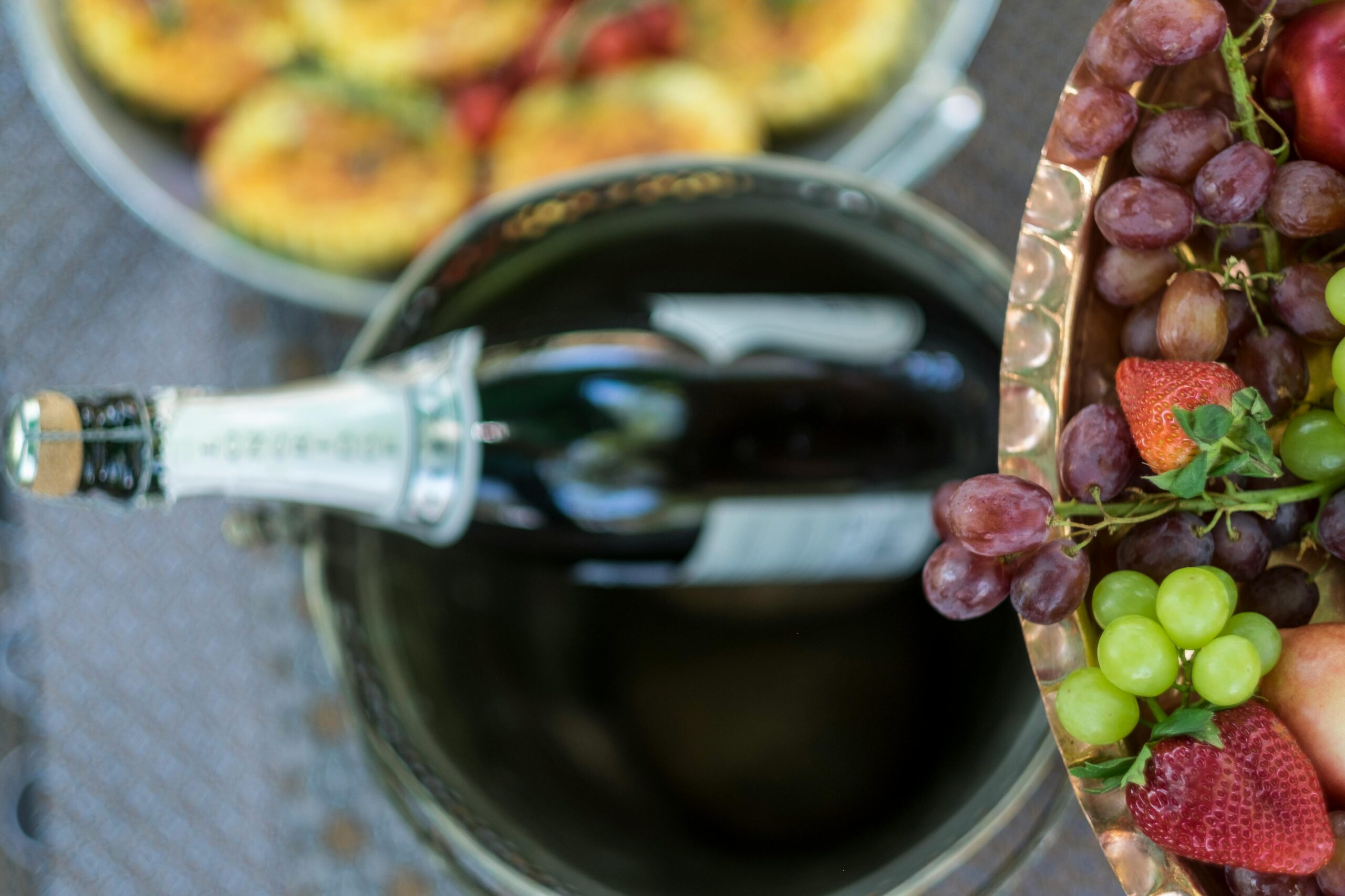 Overhead view of champagne bottle in ice bucket with fresh grapes and fruit platter on a sunny day.