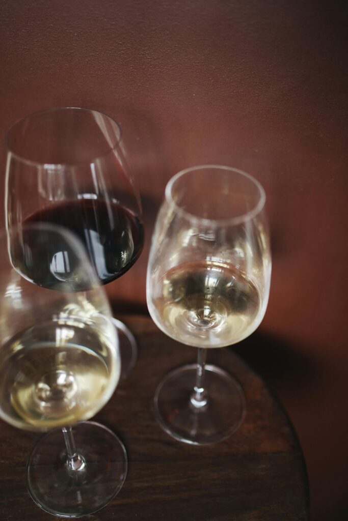 Three wine glasses with red and white wine on a rustic wooden tabletop elegantly arranged.